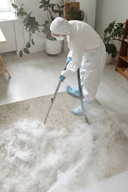 A person using a yellow and black vacuum cleaner with a long hose attachment to deep clean a patterned carpet in a residential setting. The individual's legs are visible, wearing light-colored sneaker